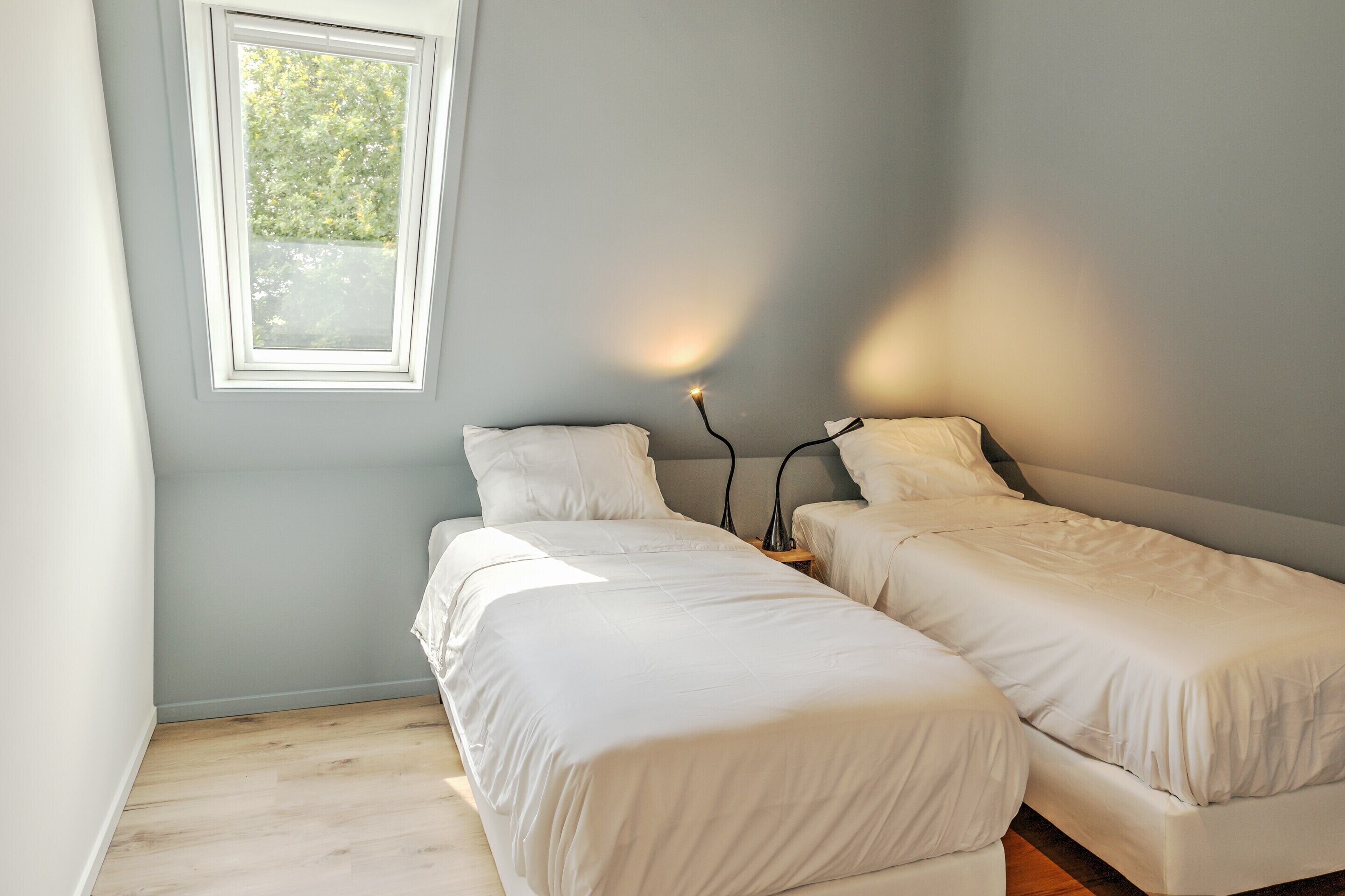 Quarto com duas camas de solteiro, mesa de cabeceira com luminária e janela com vista para o verde.