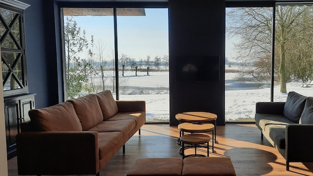 A modern living room with a large window overlooking a snowy landscape. - Tranquil Farmhouse in Rijsbergen With Hot Tub and Garden (Rijsbergen)