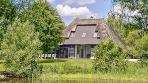 A house with a sloped roof, large windows, and a pond in the foreground. - Tranquil Farmhouse in Rijsbergen With Hot Tub and Garden (Rijsbergen)