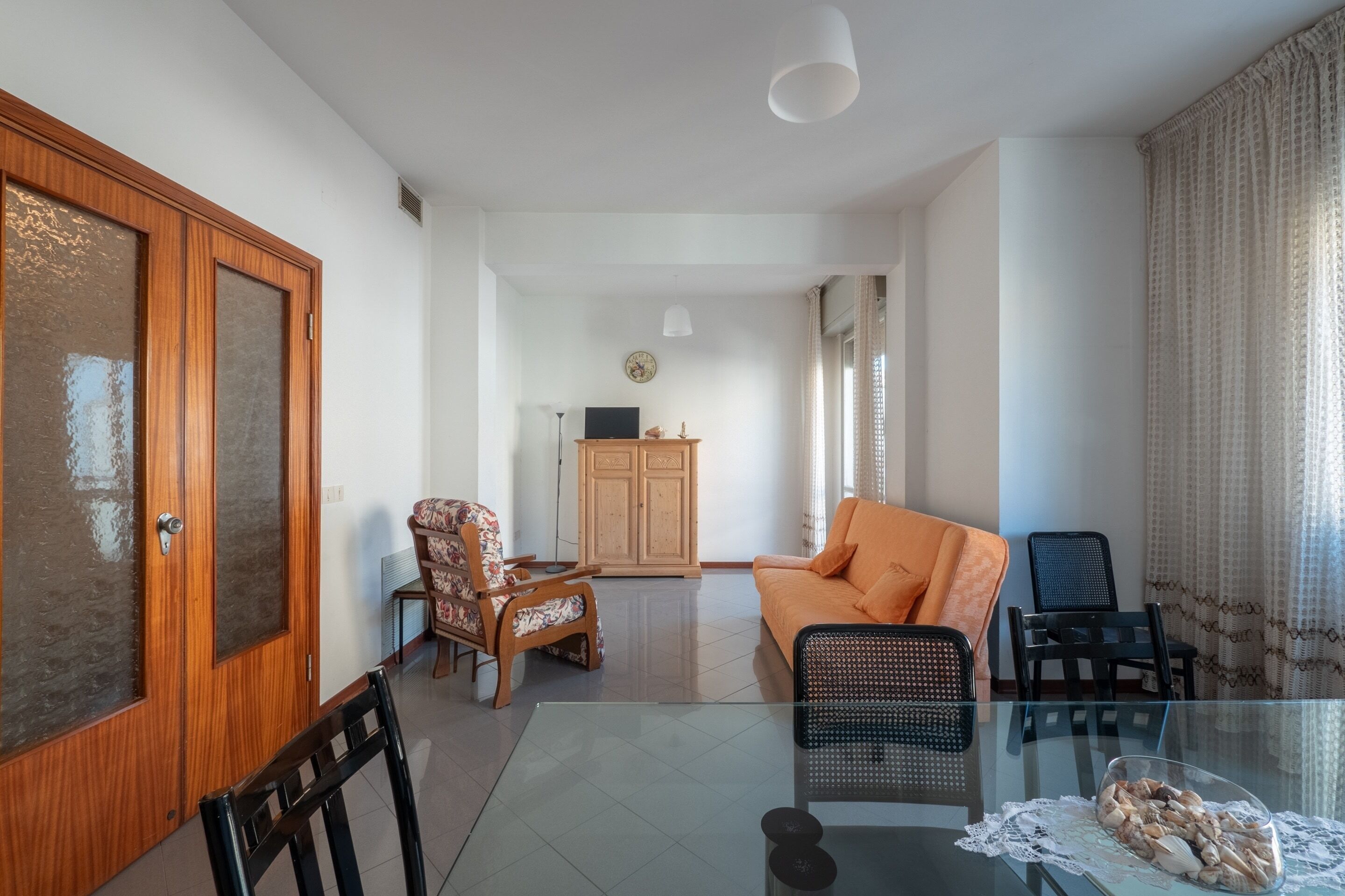 A spacious living room with a glass table, a sofa, and a wooden cabinet.