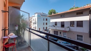 A balcony with a red chair and a small table, overlooking a street with parked cars and buildings. - Holiday Home in Fano Near the Beach (Fano)