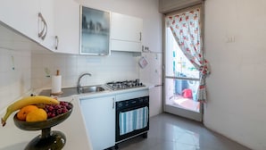 A compact kitchen with white cabinets, a gas stove, a dishwasher, and a window with a floral curtain. - Holiday Home in Fano Near the Beach (Fano)