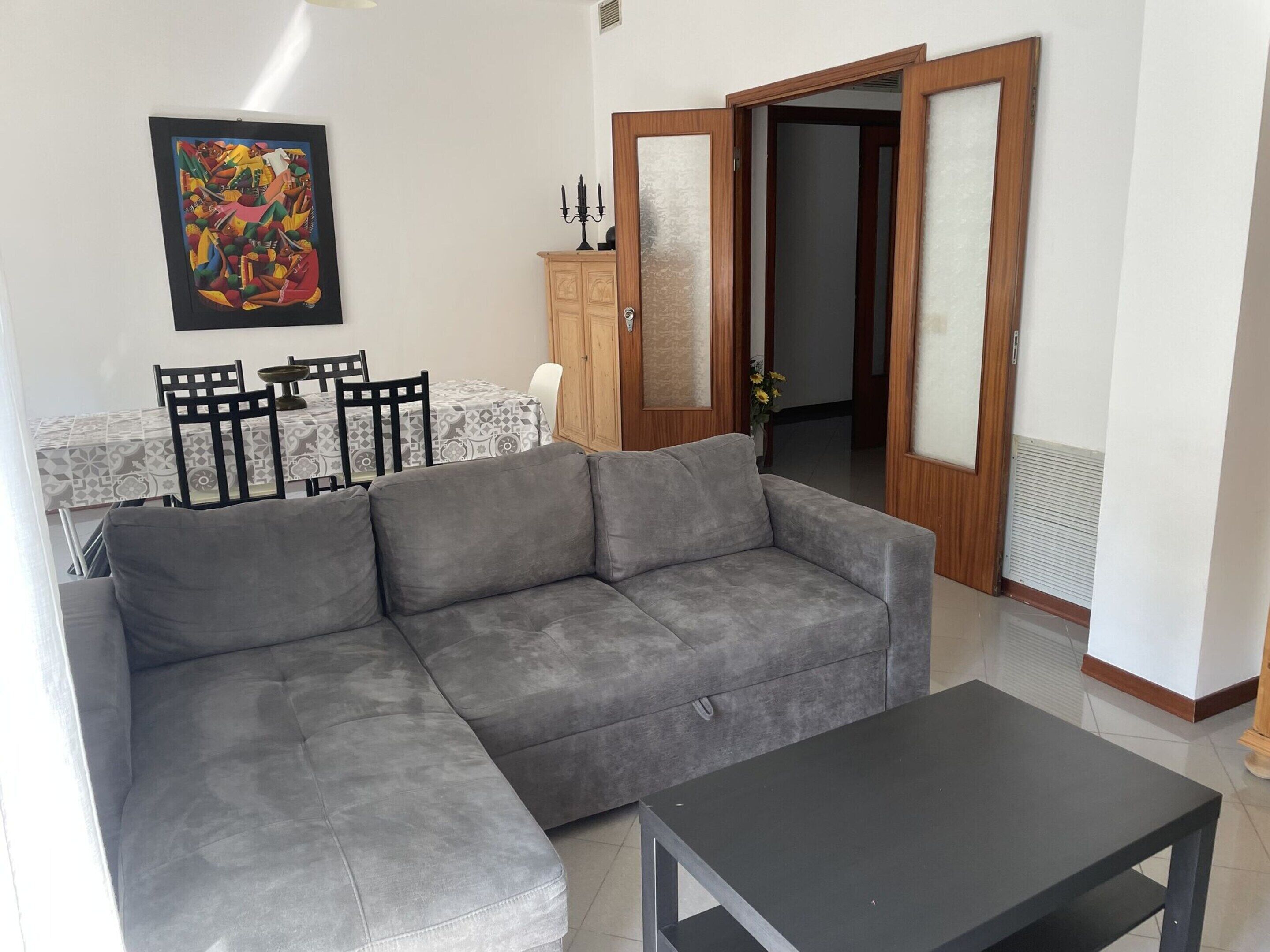 Een woonkamer met een grijze bank, een zwarte salontafel en een eethoek met een tafel en stoelen.