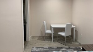 Un petit coin repas avec une table blanche et deux chaises, une porte sur la gauche et un luminaire au plafond.