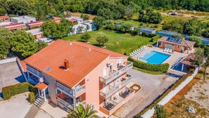 A multi-story building with a red-tiled roof, a swimming pool, and a landscaped garden. - Panoramic Apartment in Banjole near Pula Town Center (Medulin)