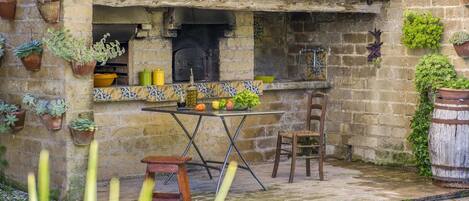 A rustic outdoor kitchen with a tiled backsplash, a brick wall, and potted plants.