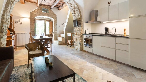 Une cuisine chaleureuse aux murs en pierre, un coin repas avec une table et des chaises, et une vue sur l’extérieur.