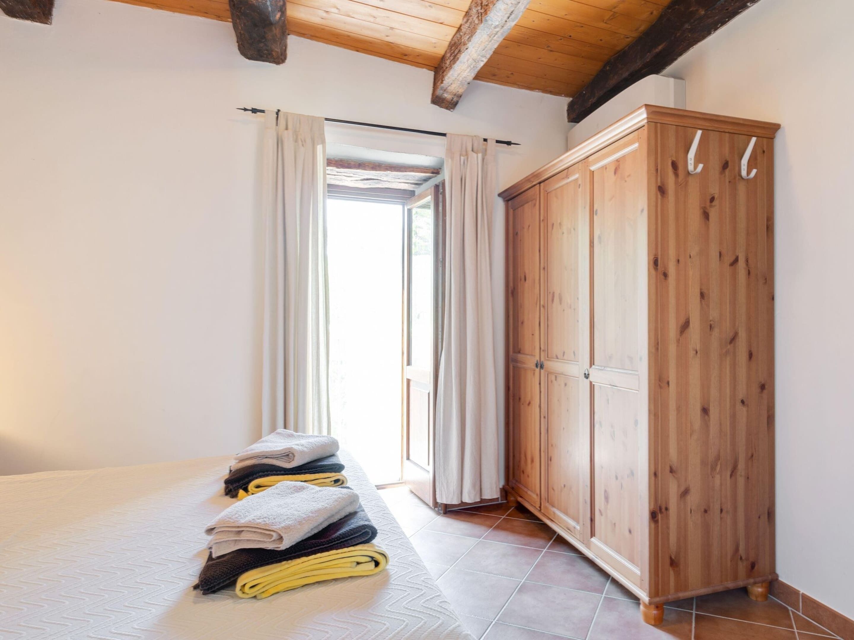 A bedroom with a bed, a wooden wardrobe, and a window with curtains.