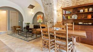 Un coin repas rustique avec un mur en pierre, des meubles en bois et une bibliothèque remplie de livres et d’ustensiles de cuisine.