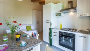 A modern kitchen with white cabinets, a gas stove, and an oven. There is a dining area with a table and chairs, and a vase with flowers on the counter.