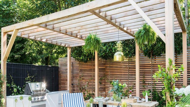 A covered outdoor patio with a grill, seating, and plants.