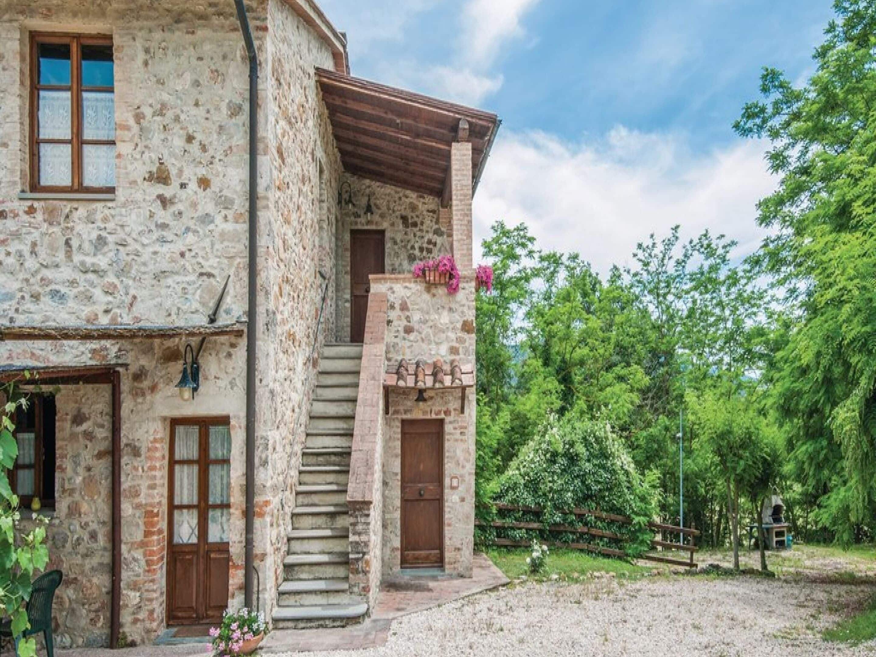 Un edificio in pietra rustica con una scala in legno che conduce a un balcone, immerso nel verde.