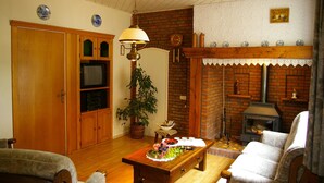Een gezellige woonkamer met houten vloeren, een open haard, een televisie en een eettafel gedekt voor twee personen.