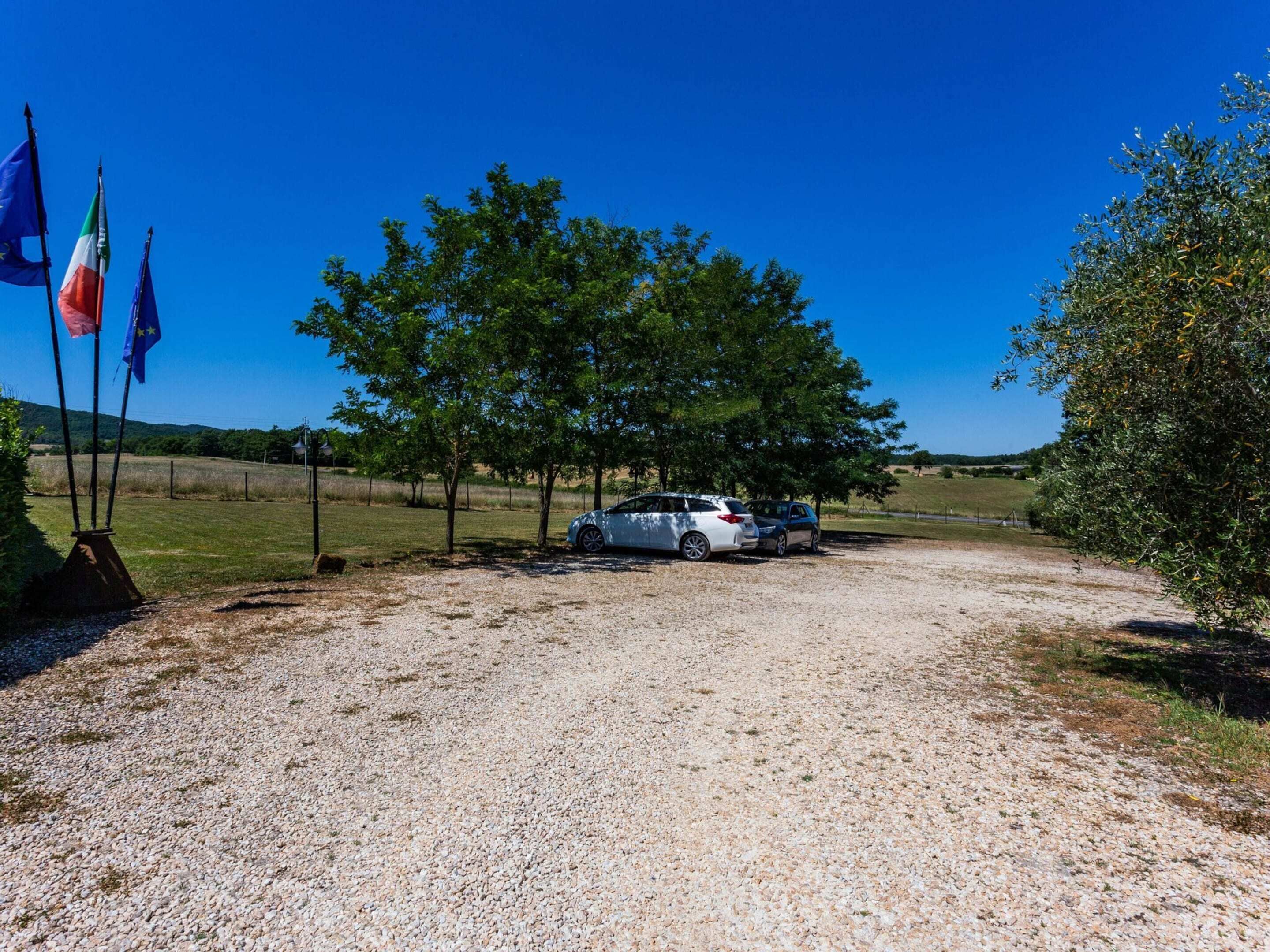 A gravel path leading to a parking area with two cars parked under trees.