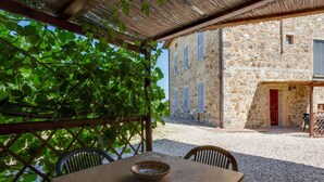 A stone building with a thatched roof patio area. - Apartment in Tuscany With Pool and Scenic Views (Casole d'Elsa)