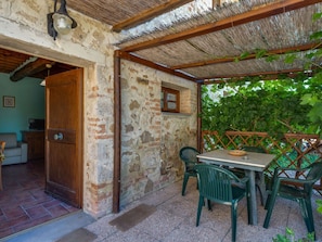 A rustic stone building with a wooden door, a small window, and a table with chairs outside.