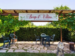 Relax in the charming outdoor seating area under a pergola, surrounded by a rustic water fountain and comfortable seating.