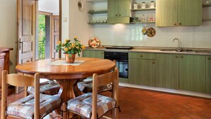 A kitchen with green cabinets, a wooden dining table with chairs, and a view of the outdoors through an open door. - Belvilla by OYO La Casa sul Fiume Piano Terra (Gallicano)