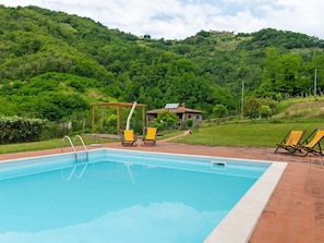 A swimming pool with two lounge chairs, a pergola, and a stone building in a lush green landscape. - Belvilla by OYO La Casa sul Fiume Piano Terra (Gallicano)
