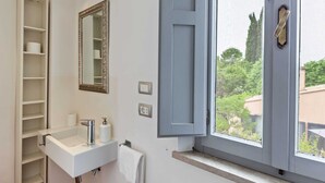 A bathroom with a white sink, a mirror, a towel rack, and a window with a view of greenery outside.