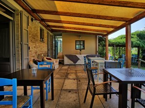 Una zona patio esterna con tavoli, sedie e un divano, addossata a un muro in mattoni.