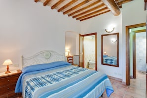 A bedroom with a bed, a nightstand, a lamp, a mirror, and a bathroom door.