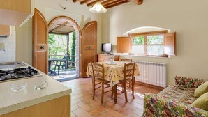 A kitchen with a stove, dining table, and chairs, a TV, and a window with curtains. - Tuscan Countryside Stay (Casole d'Elsa)