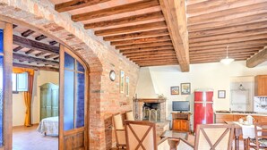 A rustic interior with exposed wooden beams, a brick fireplace, and a dining area with wooden chairs. - Belvilla by OYO Le Ginestre (Montalcino)