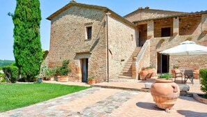 A rustic stone building with a brick patio, outdoor seating, and a tall tree. - Belvilla by OYO Le Ginestre (Montalcino)