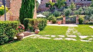 A courtyard with a stone pathway, lush green grass, and a brick building with multiple windows. - Belvilla by OYO Le Ginestre (Montalcino)
