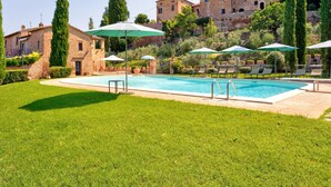 A swimming pool with lounge chairs and umbrellas, surrounded by well-maintained grass and trees. - Belvilla by OYO Le Ginestre (Montalcino)