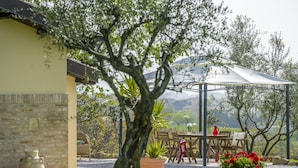 A patio area with a table and chairs, a pergola, and a view of the countryside. - Holiday Home With Swimming Pool, San Costanzo (San Costanzo)