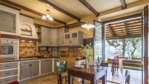 A kitchen with wooden cabinets, a dining table with chairs, and a view of the outdoors through a glass door. - Holiday Home With Swimming Pool, San Costanzo (San Costanzo)