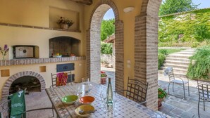 Un patio al aire libre con chimenea de ladrillo, una mesa lista para comer y vistas a un jardín y unas escaleras.