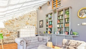 A cozy living room with a stone wall, a fireplace, and a bookshelf filled with books and decorative items.