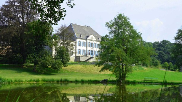 Een groot, historisch gebouw met een symmetrische gevel, een centrale ingang en een verzorgd gazon.