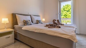 A neatly made bed with a white comforter and two decorative pillows, a bedside table with a lamp, and a view of greenery through a window. - Alluring Apartment in Banjole near Beach & Island (Medulin)