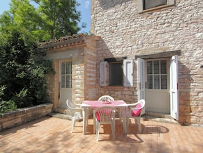 A stone building with a patio area featuring a table and chairs, a door, and a window. - Eco-retreat With Pool (Acqualagna)