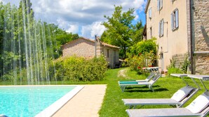 A swimming pool with a water fountain, lounge chairs, and a stone building with blue shutters. - Eco-retreat With Pool (Acqualagna)