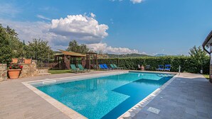 Una piscina rectangular con agua azul cristalina, rodeada por una terraza pavimentada.