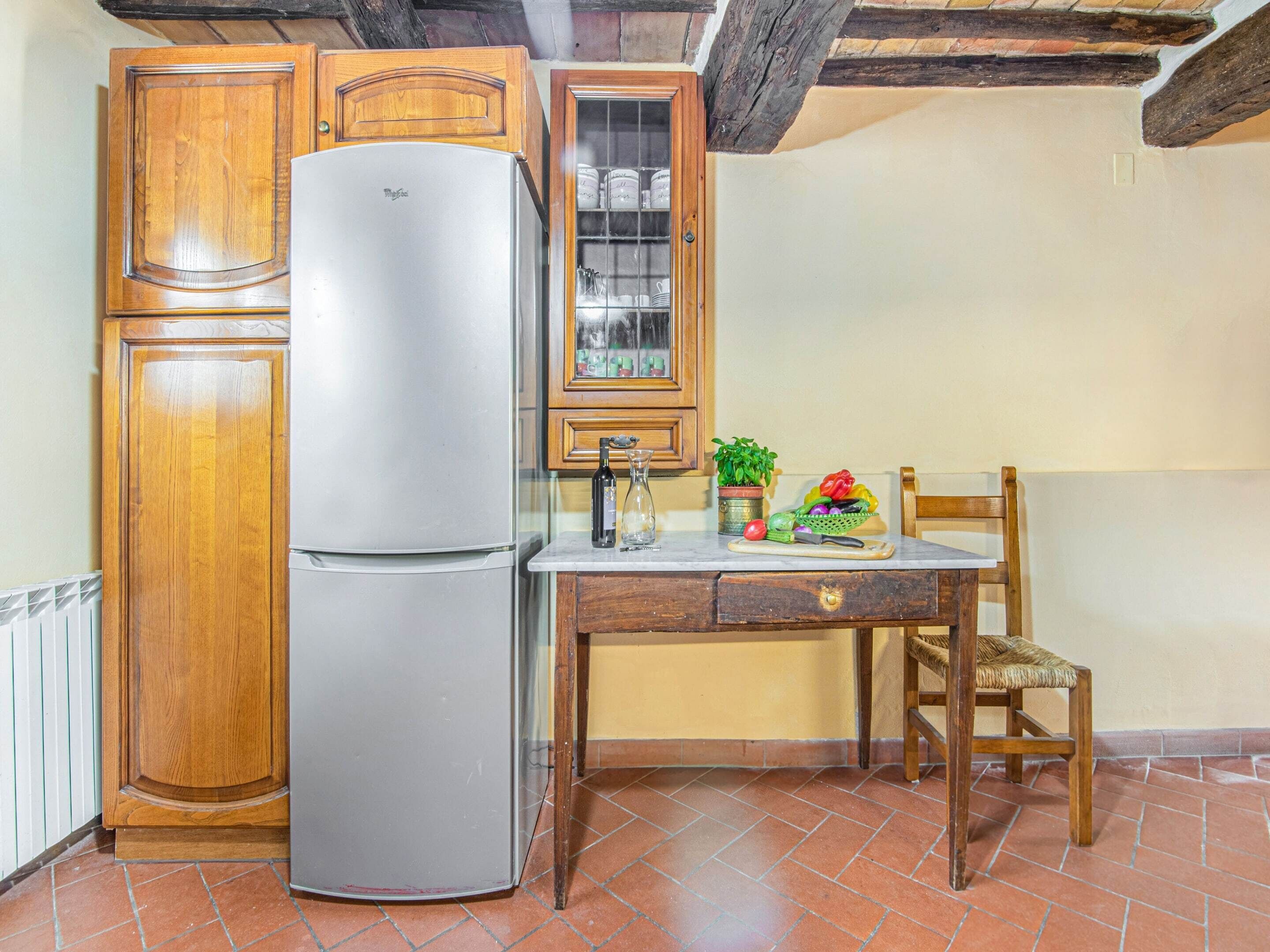 Uma cozinha com armários de madeira, uma geladeira de aço inoxidável, uma mesa de jantar de madeira com uma cadeira e um vaso com planta.