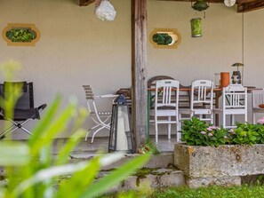 A rustic outdoor seating area with white chairs and a table, surrounded by greenery and a stone planter. - Lavish Castle in Riedenburg with Garden near Lake (Riedenburg)