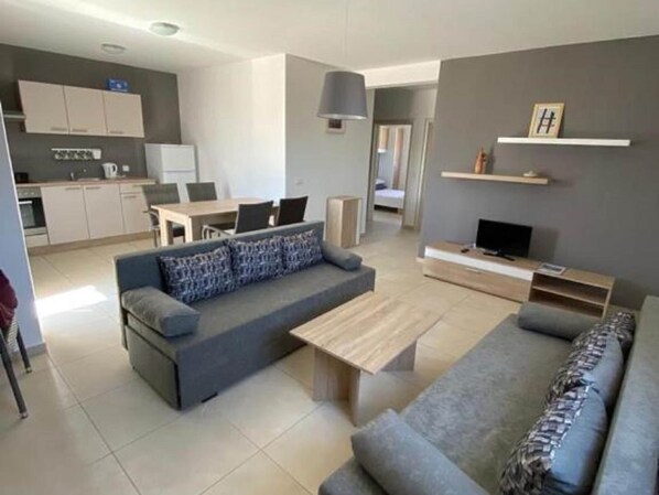 A modern living room with a grey sofa, a wooden coffee table, and a TV stand.