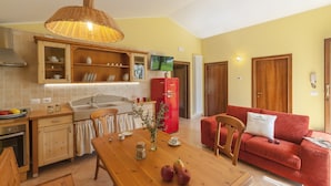 A modern kitchen with wooden cabinets, a red refrigerator, a dining table with apples, and a red sofa in a bright living area. - Beautiful Holiday Home With Covered Terrace (San Costanzo)