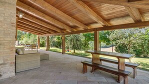 An outdoor covered patio with stone flooring, wooden benches, and a brick wall. - Villa in Piandimeleto With Pool & Sauna (Piandimeleto)