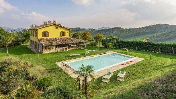 A yellow villa with a swimming pool, surrounded by lush greenery and hills in the background. - Villa in Piandimeleto With Pool & Sauna (Piandimeleto)