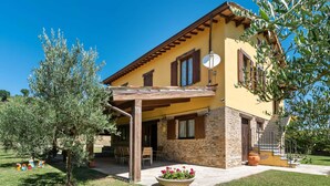 A two-story house with a stone facade, a wooden pergola, and a garden with a flower bed. - Villa in Piandimeleto With Pool & Sauna (Piandimeleto)