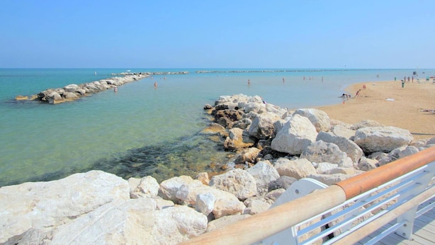 A beach with clear water, rocky shore, and a wooden railing.