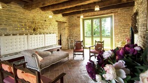 A rustic room with stone walls, a wooden ceiling, a bench, two chairs, and a large window.