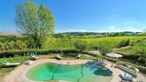 A pool area with lounge chairs and a seating area, surrounded by a landscaped garden and a vineyard in the background.
